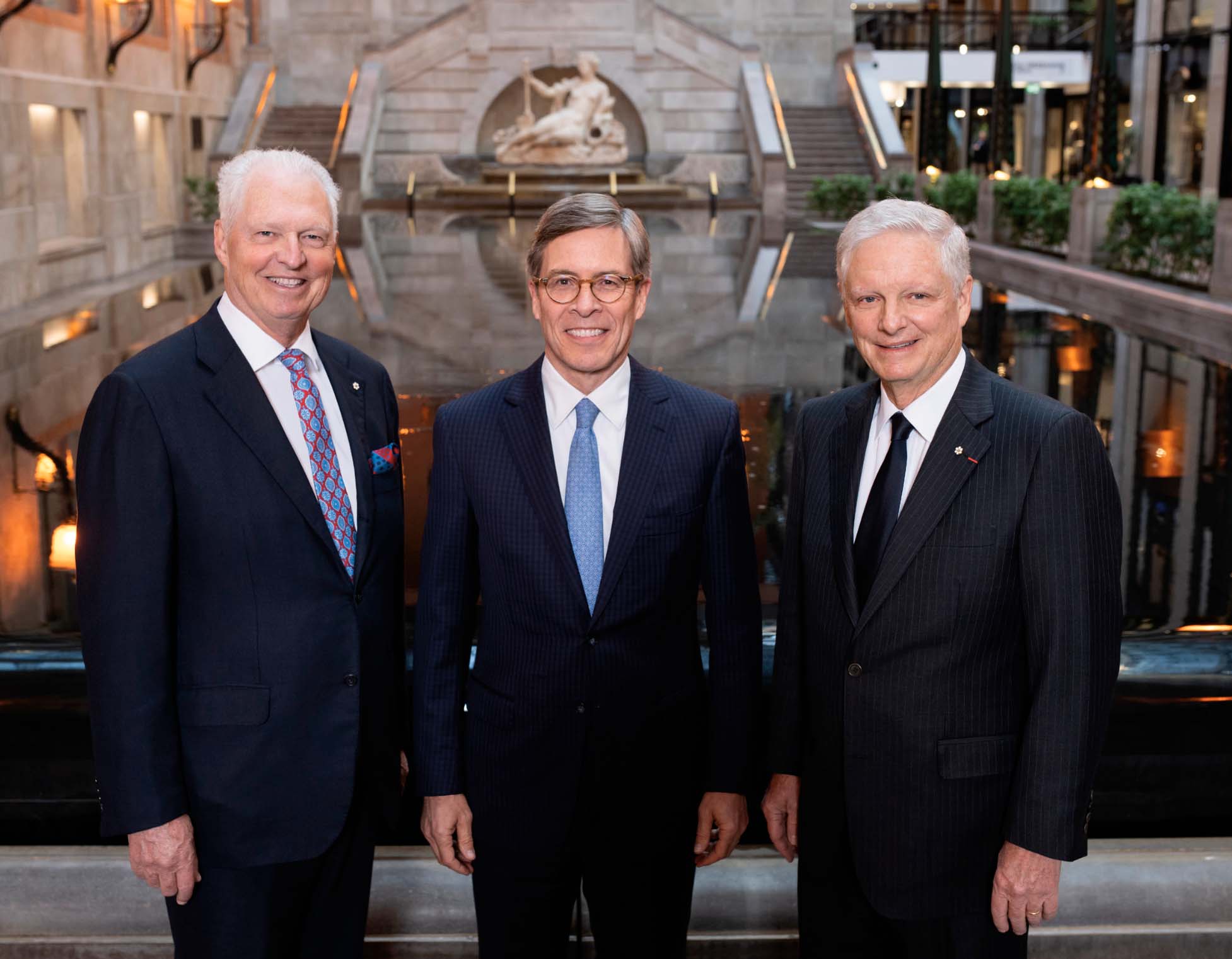 A photograph of three men in suits, in front of a fountain. The men are, from left to right: André Desmarais, Jeffrey Orr and Paul Desmarais, Jr.